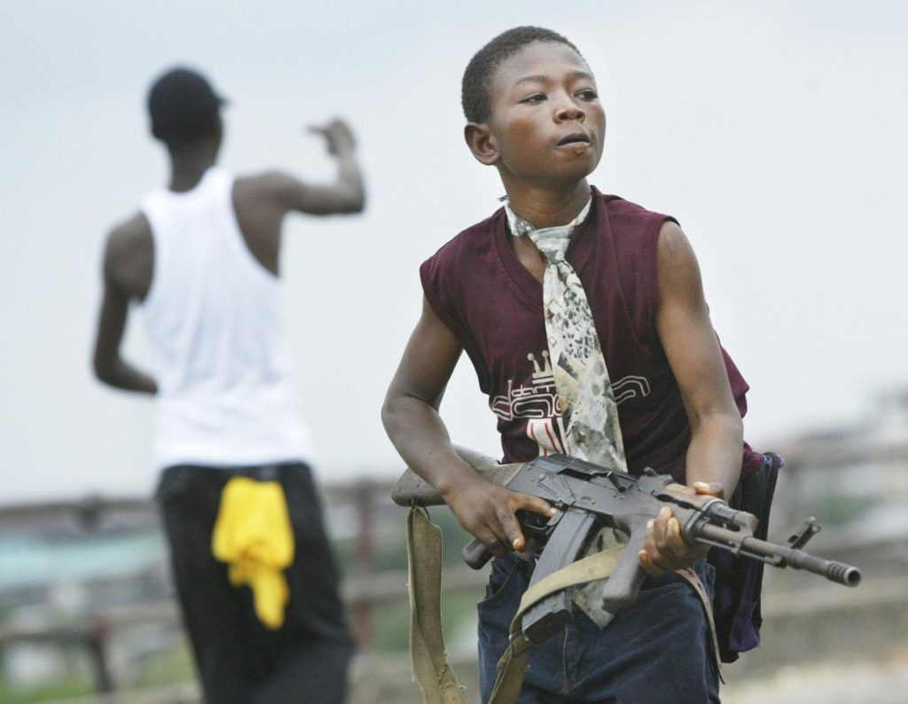 MONROVIA, LIBERIA - JULY 30 - A child Liberian militia soldier loyal to the government walks away from firing while another taunts them on July 30, 2003 in Monrovia, Liberia. Sporadic clashes continue between government forces and rebel fighters in the fight for control of Monrovia.